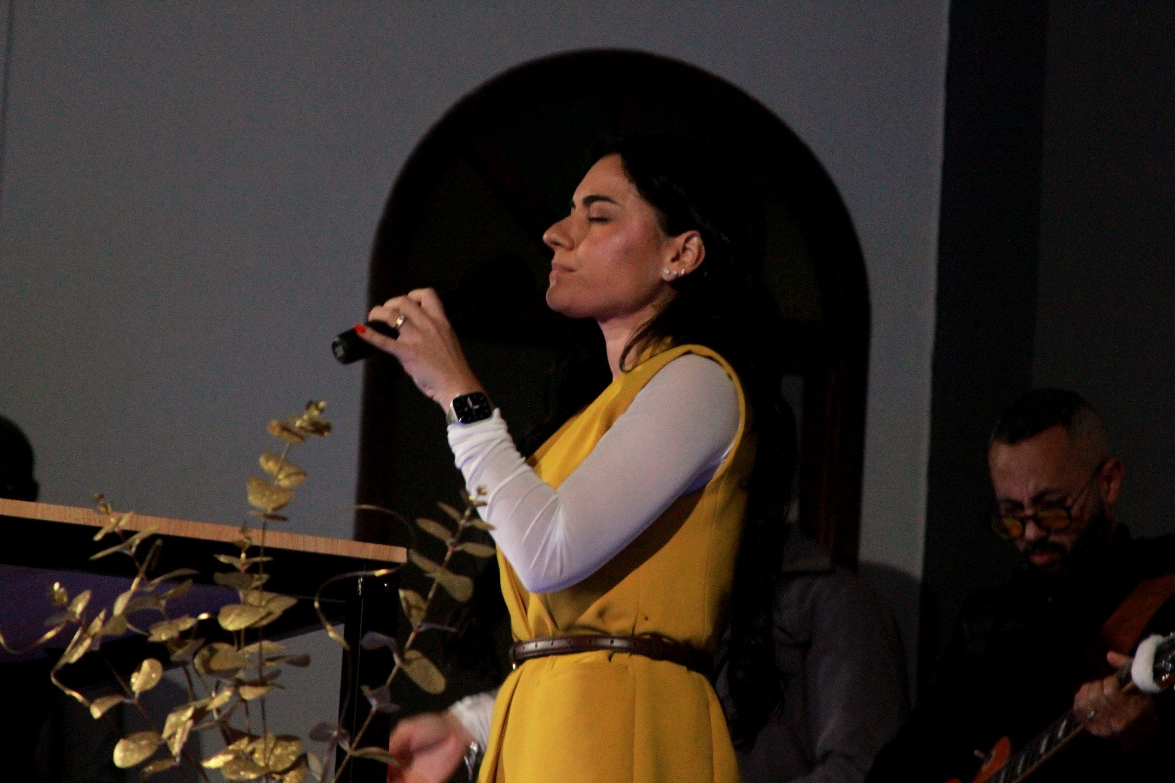 Uma cantora do louvor, de olhos fechados, à frente do arco do púlpito